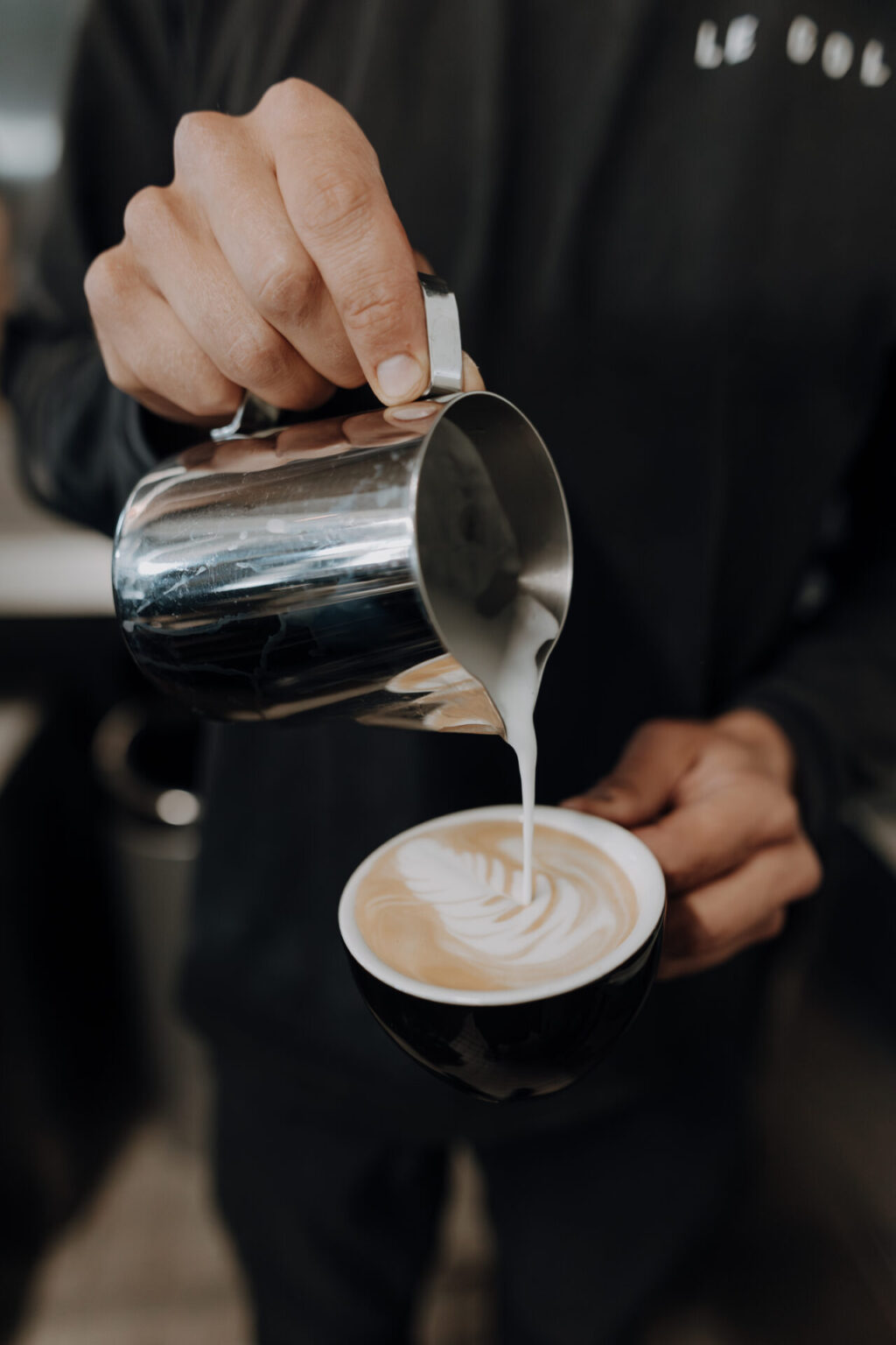 Barista gießt Milch in einen Cappuccino
